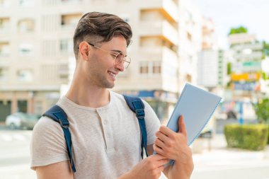 Genç ve yakışıklı bir öğrenci açık havada mutlu bir ifadeyle.