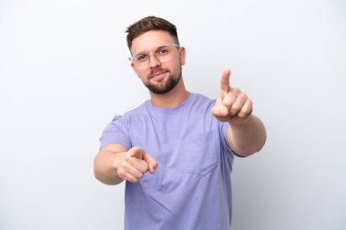 Beyaz arka planda izole edilmiş genç beyaz adam mutlu bir ifadeyle ön tarafı işaret ediyor.