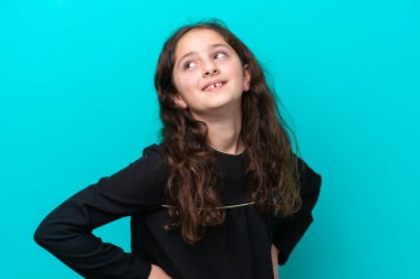 Mavi arka planda izole edilmiş küçük bir kız kolları kalçasında poz veriyor ve gülümsüyor