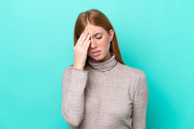 Genç kızıl saçlı kadın mavi arka planda baş ağrısı ile izole edilmiş.