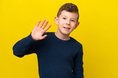 Sarı arka planda izole edilmiş küçük beyaz çocuk mutlu bir ifadeyle selamlıyor.