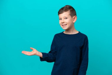 Küçük çocuk mavi arka planda izole edilmiş bir şekilde gülümserken bir fikir sunuyor.