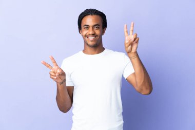 Örgülü genç Afrikalı Amerikalı adam mor arka planda izole edilmiş iki eliyle zafer işareti gösteriyor.