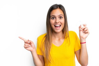 Beyaz arka planda izole edilmiş görünmez diş telleri tutan genç beyaz kadın şaşırmış ve parmağıyla kenarı işaret ediyor.