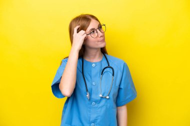 Sarı arka planda izole edilmiş genç kızıl saçlı hemşirenin şüpheleri var ve kafası karışmış bir yüz ifadesi var.