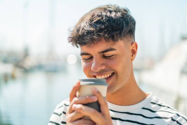 Dışarıdaki İspanyol genç adam elinde neşeli bir ifadeyle kahveyi tutuyor.