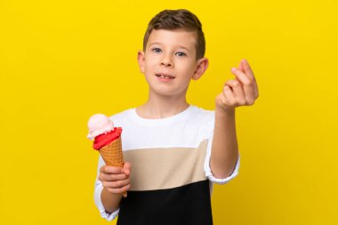 Sarı arka planda izole edilmiş kornet dondurması olan beyaz bir çocuk para hareketi yapıyor.