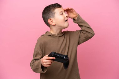 Pembe arka planda izole edilmiş bir bilgisayar oyunu kontrolörüyle oynayan beyaz bir çocuk.