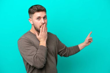 Young caucasian man isolated on blue background with surprise expression while pointing side