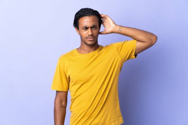 Örgülü genç Afrikalı Amerikalı adam mor arka planda izole edilmiş. Kafasını kaşırken şüpheleri var.
