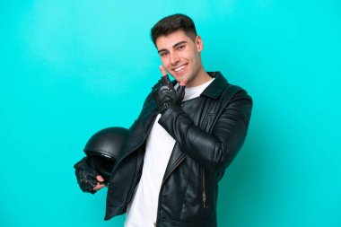 Motosiklet kasklı genç beyaz adam mavi arka planda izole edilmiş mutlu ve gülümsüyor.