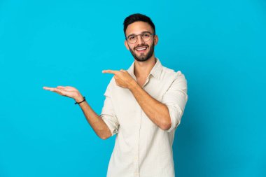 Mavi arka planda izole edilmiş genç beyaz adam bir ilan vermek için avucunun içinde hayali bir fotokopi makinesi tutuyor.