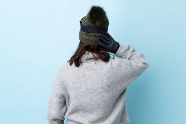 Karma kayakçı kız, snowboard gözlükleriyle arka planda izole edilmiş mavi arka planda ve düşünüyor..