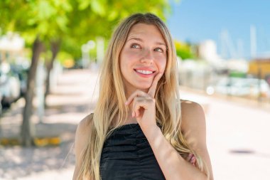 Açık havada genç sarışın bir kadın yukarı bakarken bir fikir düşünüyor.