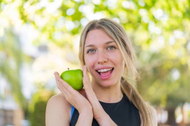 Açık havada, elinde elma tutan genç sarışın kadın.