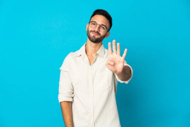 Mavi arka planda izole edilmiş genç beyaz adam mutlu ve parmaklarıyla dört tane sayıyor.