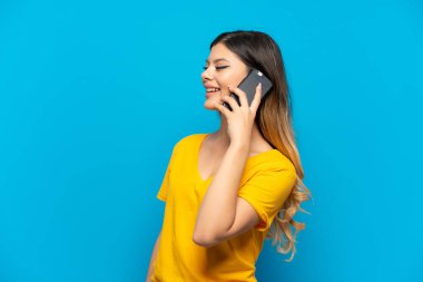 Mavi arka planda izole edilmiş genç bir Rus kız cep telefonuyla sohbet ediyor.