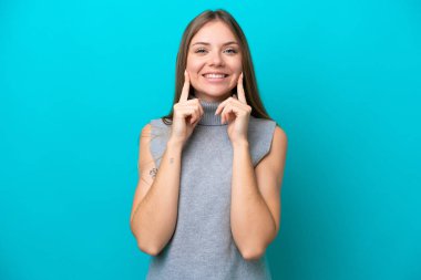 Genç Litvanyalı kadın mavi arka planda izole edilmiş mutlu ve hoş bir ifadeyle gülümsüyor.