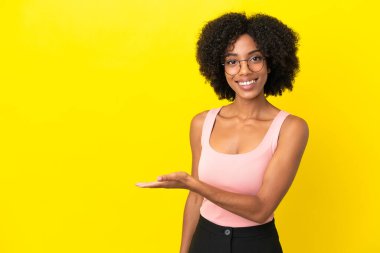 Sarı arka planda izole edilmiş genç Afrikalı Amerikalı bir kadın gülümseyerek bir fikir sunuyor.