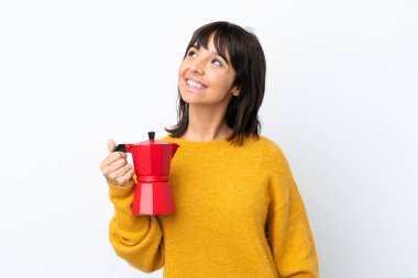 Beyaz arka planda kahve demliği tutan genç melez kadın yukarı bakarken bir fikir düşünüyor.