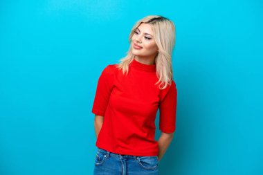 Genç Rus kadın mavi arka planda izole edilmiş, yan tarafa bakıyor ve gülümsüyor.