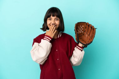 Beyzbol eldivenli genç ve melez bir bayan mavi arka planda izole edilmiş mutlu ve ağzı kapalı gülümsüyor.