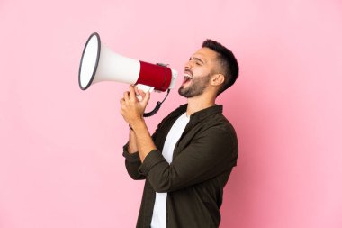 Pembe arka planda izole edilmiş genç beyaz bir adam megafondan bir şey duyurmak için bağırıyor.