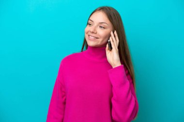 Genç Litvanyalı bir kadın mavi arka planda izole edilmiş. Cep telefonuyla biriyle sohbet ediyor.