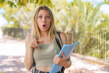 Açık havada genç sarışın bayan şaşırmış ve ön tarafı işaret ediyor.