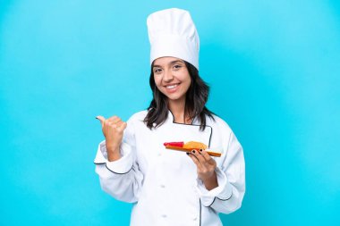 Mavi arka planda saşimi tutan genç İspanyol aşçı kadın bir ürünü sunmak için kenarı işaret ediyor.