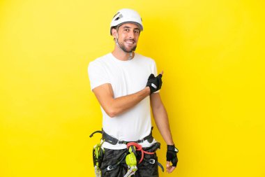 Genç kaya tırmanışçısı sarı arka planda izole edilmiş geriye doğru işaret ediyor.