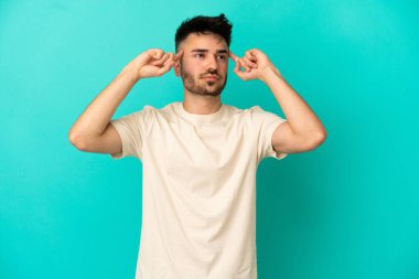 Kafkasyalı genç adam mavi arka planda izole edilmiş. Şüpheleri ve düşünceleri var.