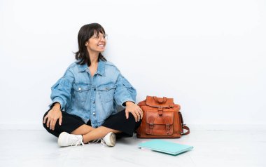 Genç bir kız öğrenci, beyaz arka planda, izole bir katta oturuyor.