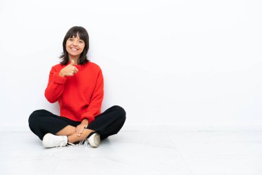 Genç, melez bir kadın, beyaz arka planda izole bir şekilde yerde oturuyor.