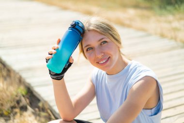 Açık havada bir şişe suyla spor yapan genç sarışın kadın.