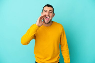 Mavi arka planda izole edilmiş yakışıklı beyaz adam ağzı açık bağırıyor.