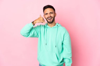 Pembe arka planda izole edilmiş genç beyaz bir adam telefon jesti yapıyor. Bana geri dönüş işareti ver.