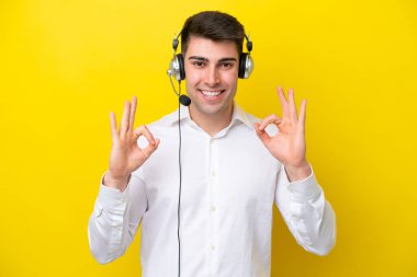 Tele pazarlamacı beyaz adam sarı arka planda izole edilmiş bir kulaklıkla çalışıyor.