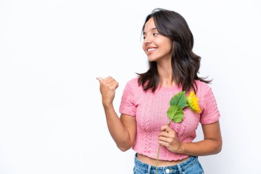 Beyaz arka planda izole edilmiş ayçiçeği tutan genç İspanyol kadın bir ürünü sunmak için kenarı işaret ediyor.