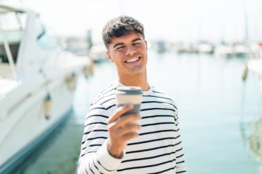 Genç İspanyol adam elinde kahveyle dışarıda mutlu bir ifadeyle bekliyor.