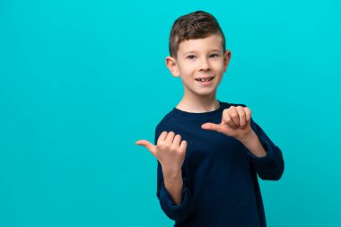 Mavi arka planda izole edilmiş küçük çocuk bir ürünü sunmak için yan tarafı işaret ediyor.