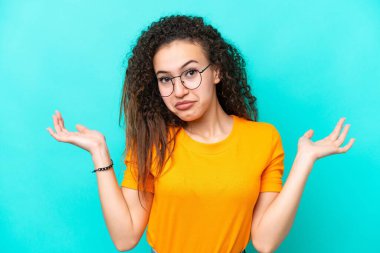 Mavi arka planda, gözlüklü ve kuşkulu genç bir Arap kadın.