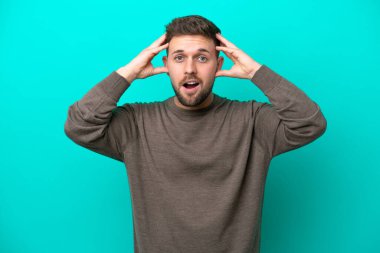 Mavi arka planda mahsur kalmış beyaz bir genç, sürpriz bir ifadeyle.