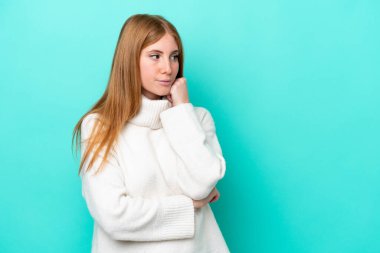 Genç kızıl saçlı kadın mavi arka planda soyutlanmış, yorgun ve sıkılmış bir ifadeyle.