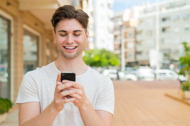 Genç yakışıklı adam cep telefonuyla mesaj ya da e-posta yolluyor.