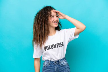 Genç Arap gönüllü kadın mavi arka planda izole edilmiş, çok gülümsüyor.