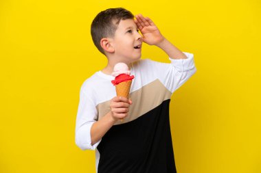 Sarı arka planda izole edilmiş kornet dondurması olan beyaz bir çocuk çok gülümsüyor.