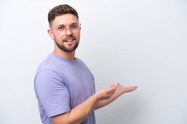 Beyaz arka planda soyutlanmış beyaz tenli genç adam davet edilmek için ellerini yana uzatıyor.