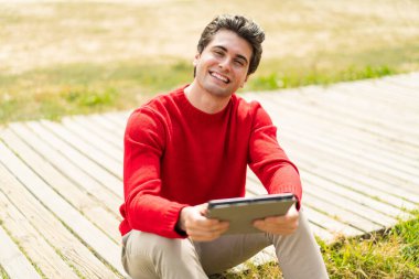 Genç yakışıklı bir adam elinde tabletle dışarıda mutlu bir ifadeyle bekliyor.