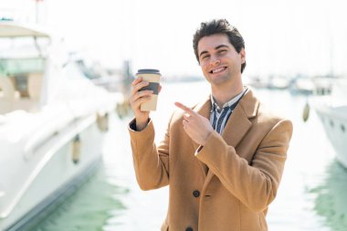 Genç yakışıklı bir adam açık havada kahve tutuyor ve onu doğrultuyor.